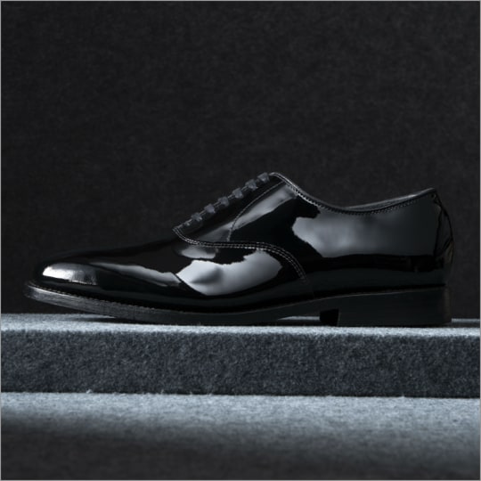 A side view of a black patent leather oxford dress shoe with the toe facing left.