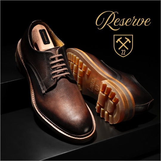 A pair of brown leather derby dress shoes, with one shoe laying on its side to highlight the lug sole. The Allen Edmonds Reserve logo is shown in the top right corner.