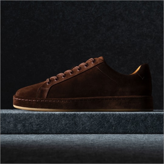 A side view of a brown suede men’s sneaker with the toe facing left.