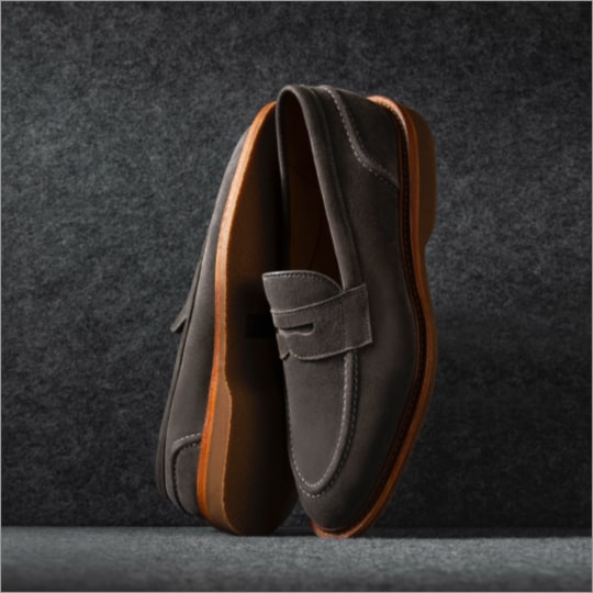 A pair of grey suede loafers displayed vertically, with one sole facing forward.