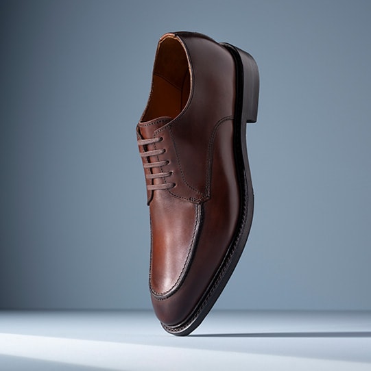 A pair of gray suede penny loafers displayed vertically, with one sole facing forward.